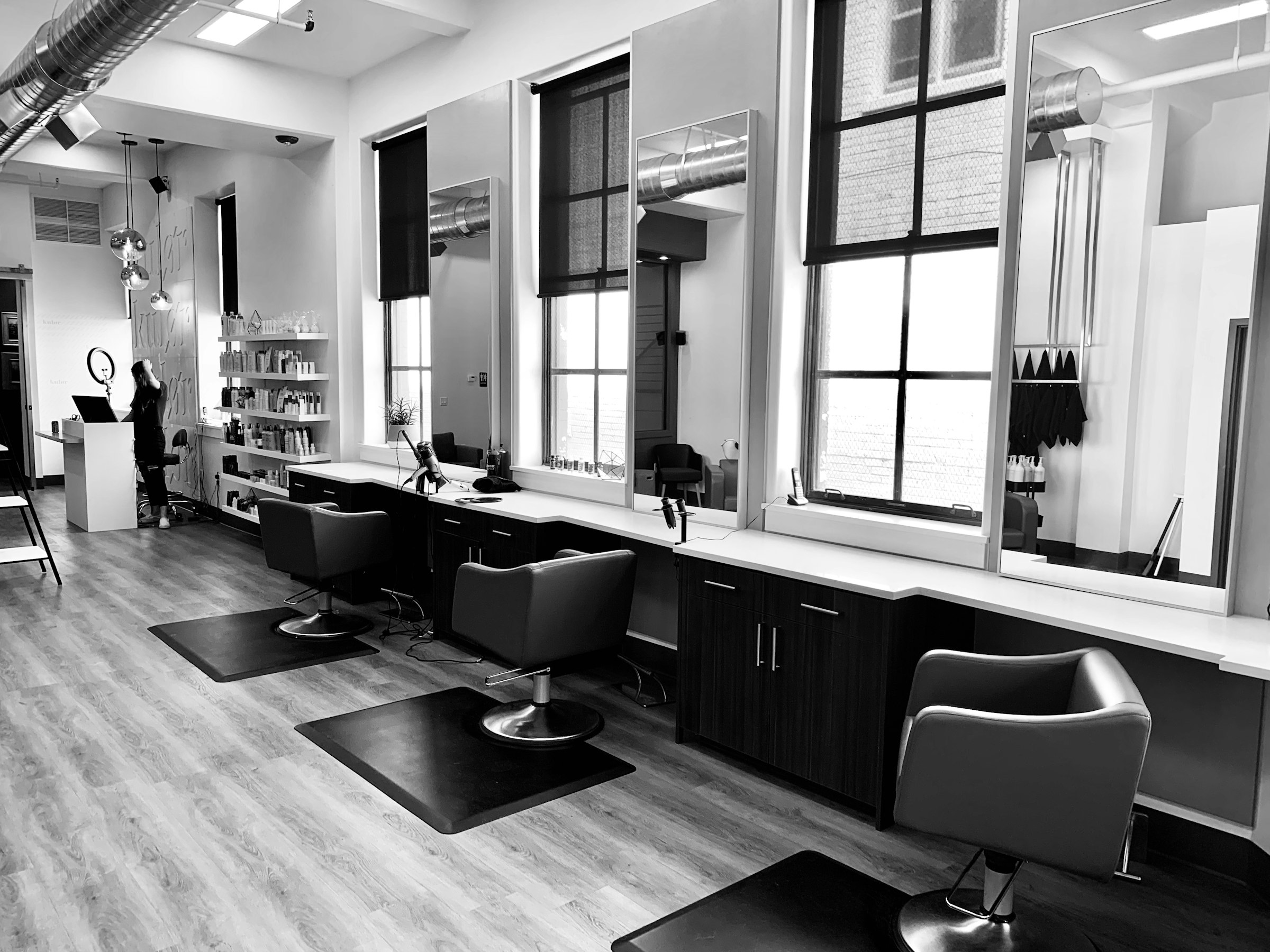 A modern salon interior. Empty styling chairs, large mirrors, the floor a host walks before the first client of the day.